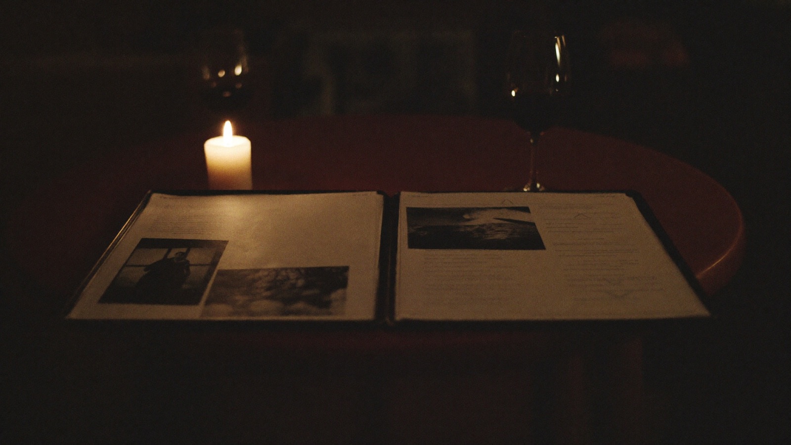 A candlelit table for two with an open murder mystery case file between two glasses of red wine