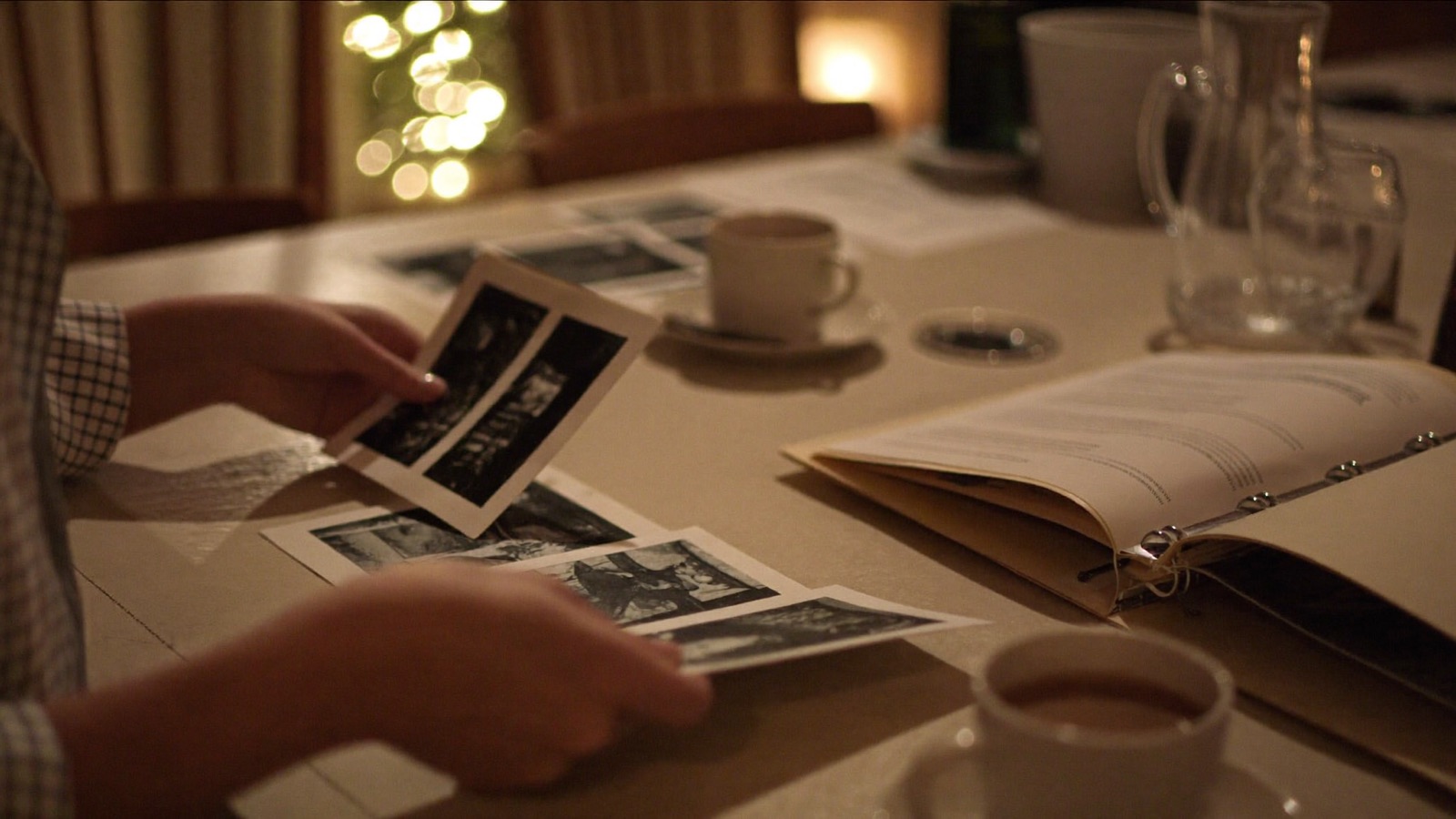 Adult and child hands examining evidence photographs from a murder mystery case file at a warm kitchen table